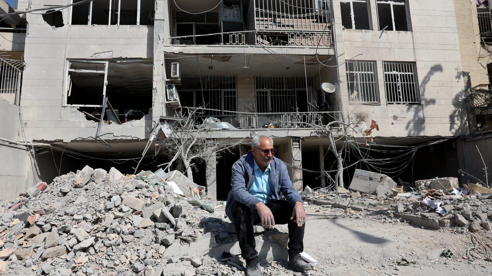An Iranian man sits next to the damaged remains of his residential building in central Tehran, Iran, 04 March 2026.