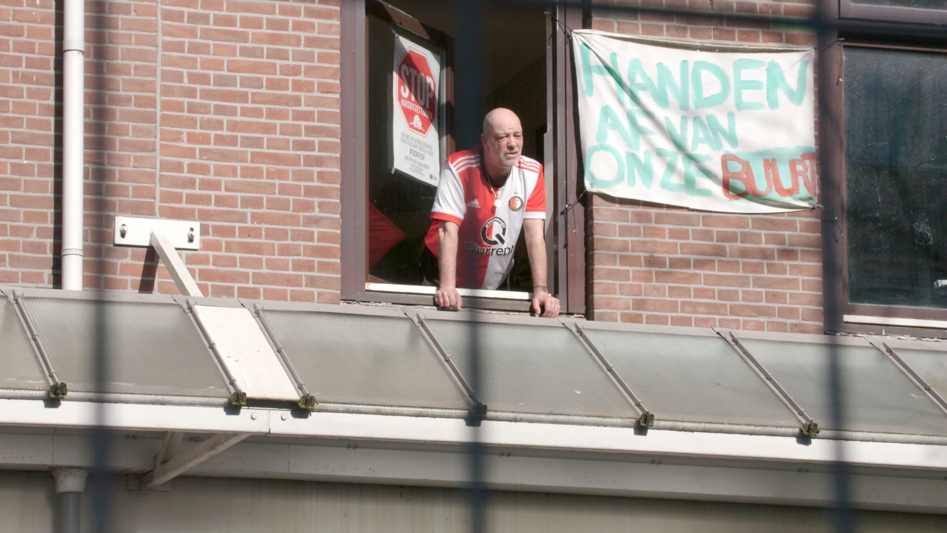 Man hangt uit het raam met spandoek 'Handen af van onze buurt', in Tweebos Rotterdam